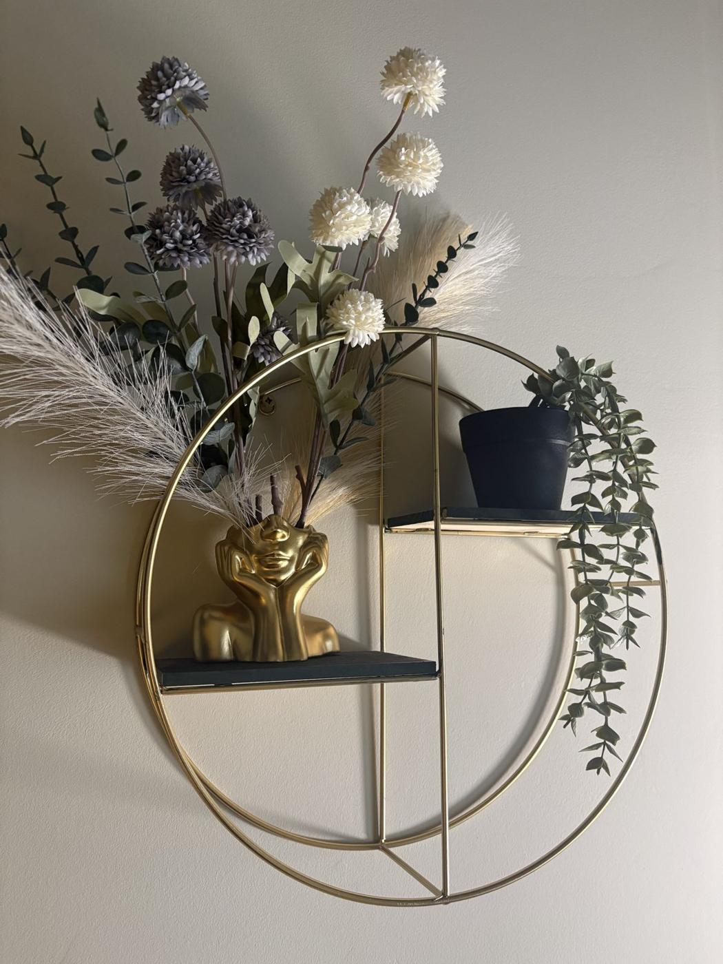 A round gold shelf with a sculpted vase and soft dried flowers in our counselling room