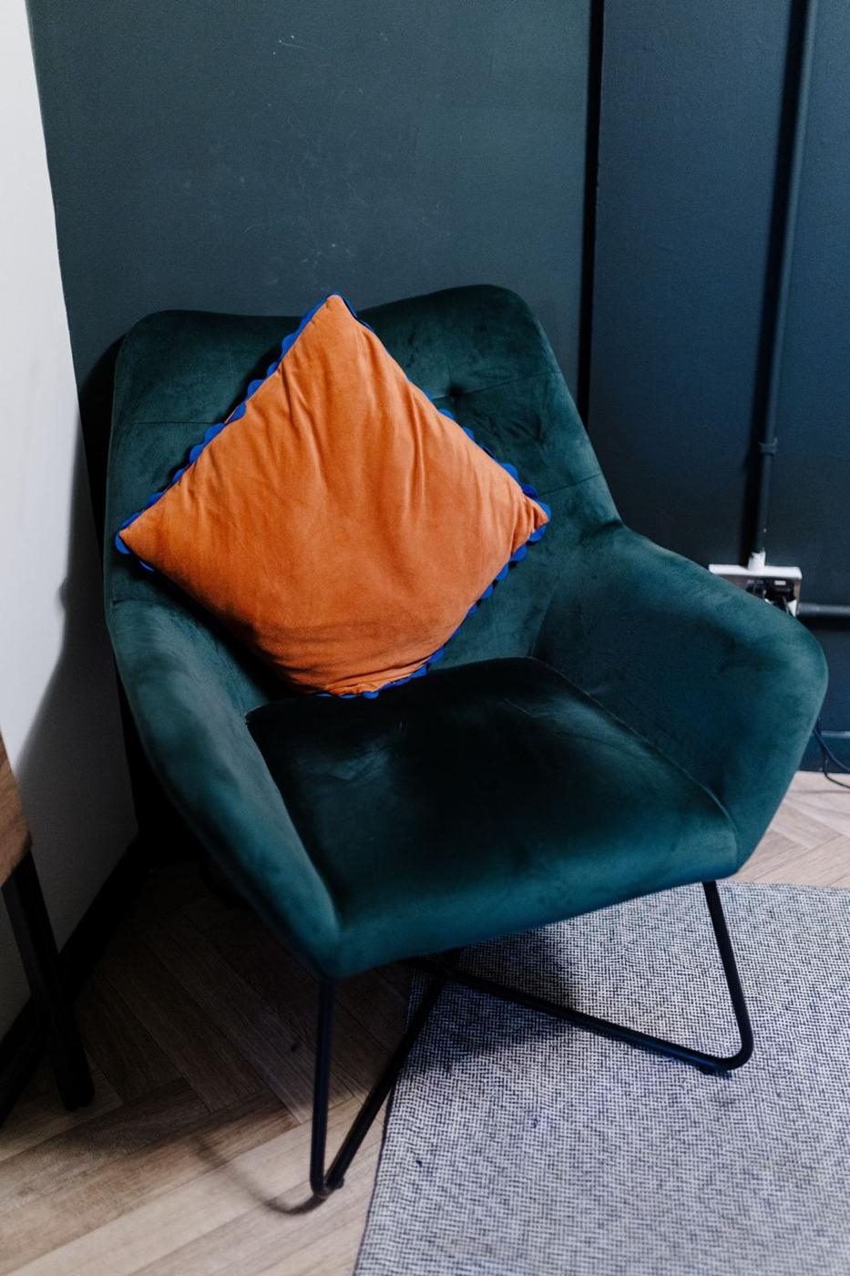 A green velvet armchair with an orange cushion in our counselling room