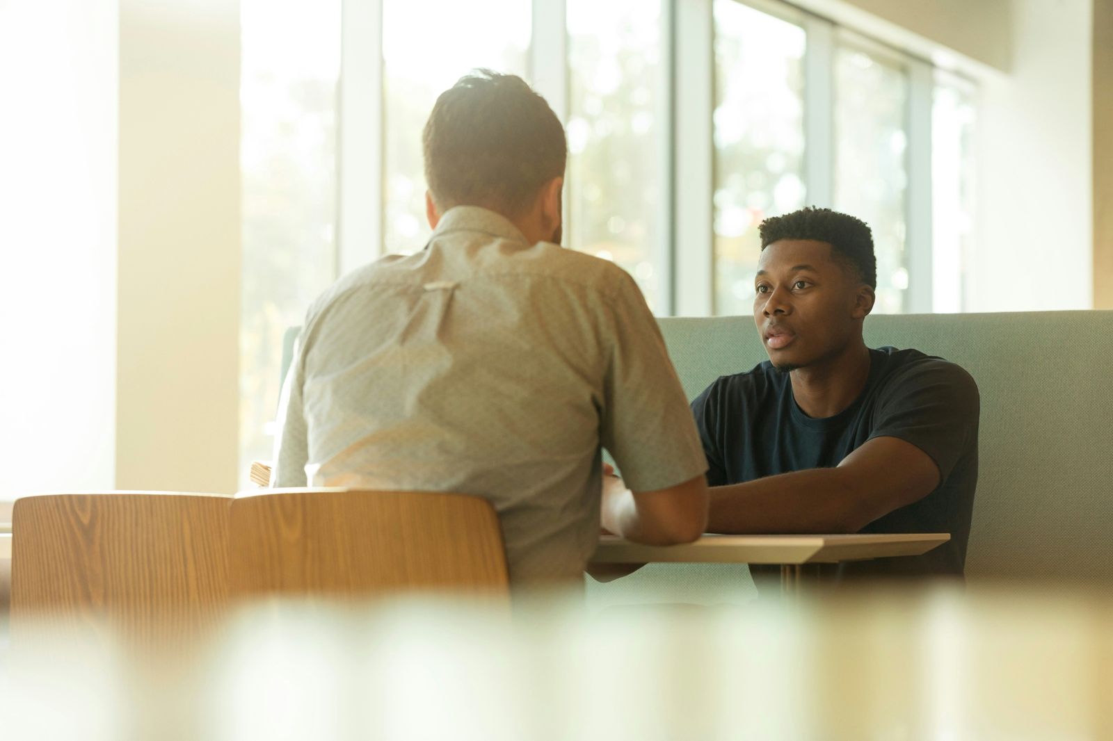 Two men in conversation at a table by a sunlit window